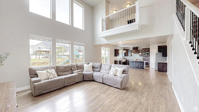living room with stairway, light wood-type flooring, a towering ceiling, and baseboards