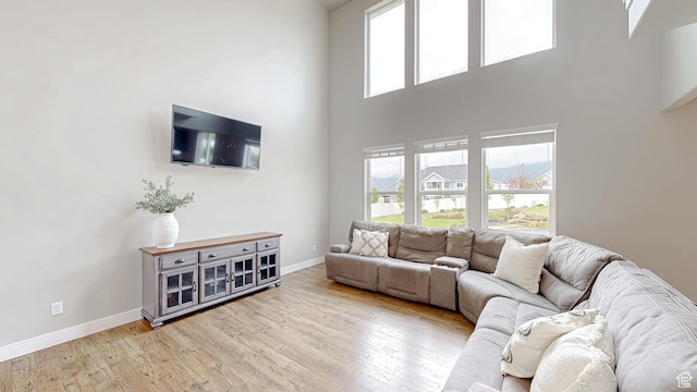 living area featuring baseboards, plenty of natural light, a towering ceiling, and light wood finished floors