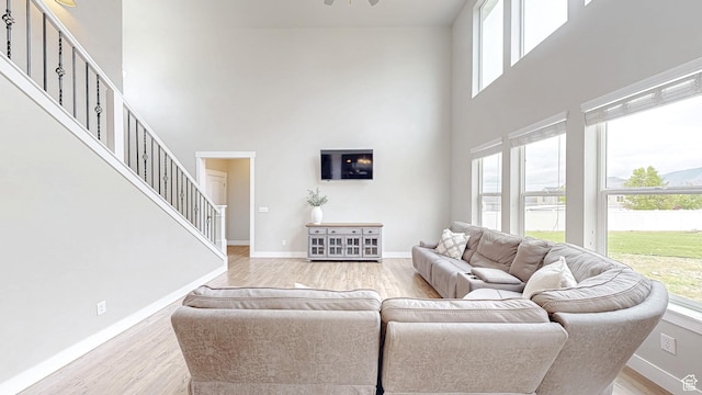 living room featuring a towering ceiling, plenty of natural light, stairway, light wood-style flooring, and baseboards
