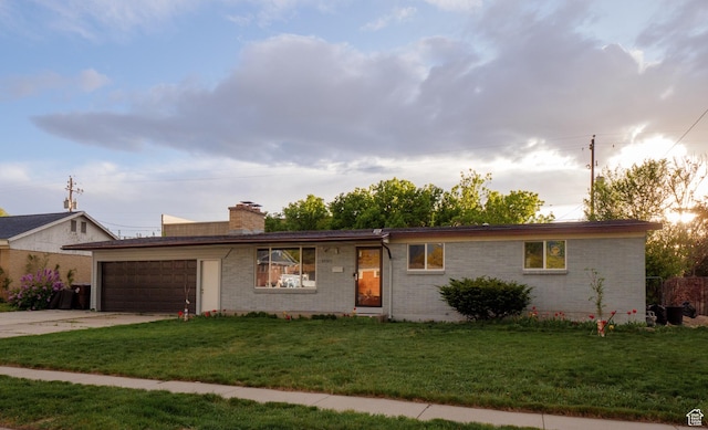 ranch-style house featuring an attached garage, a front yard, driveway, a chimney, and brick siding