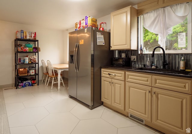 kitchen with stainless steel refrigerator with ice dispenser, a sink, dark countertops, and cream cabinetry