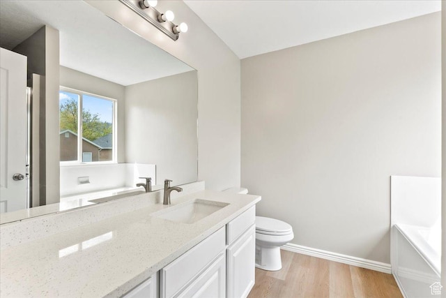bathroom with wood finished floors, toilet, baseboards, vanity, and a tub