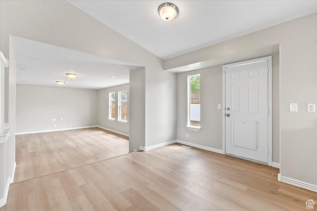 entryway featuring light wood finished floors, vaulted ceiling, plenty of natural light, and baseboards