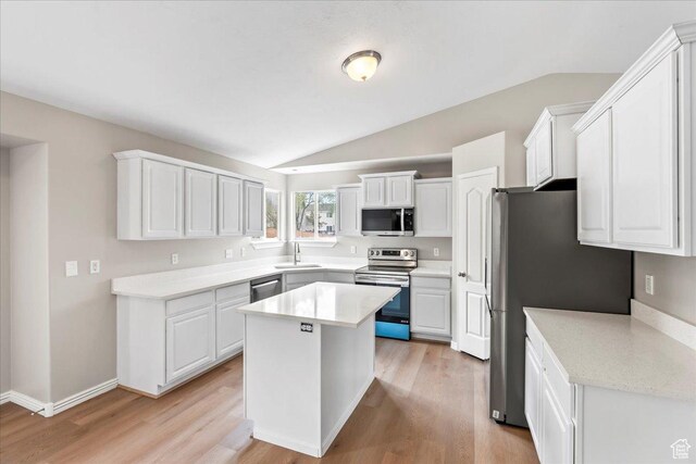 kitchen with appliances with stainless steel finishes, vaulted ceiling, a sink, light countertops, and a center island