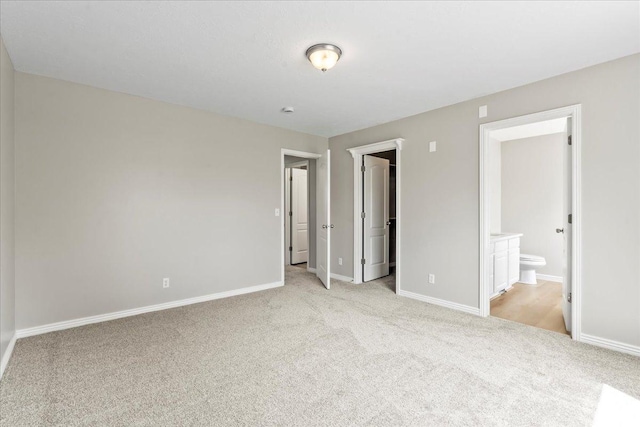 unfurnished bedroom with light carpet, baseboards, and ensuite bath