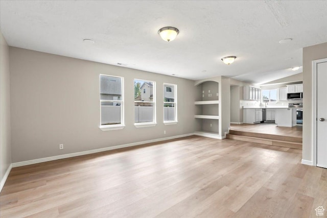 unfurnished living room featuring baseboards, light wood-style flooring, a textured ceiling, and built in shelves