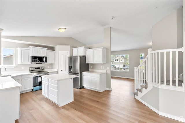kitchen with stainless steel appliances, a sink, light wood-type flooring, lofted ceiling, and white cabinets