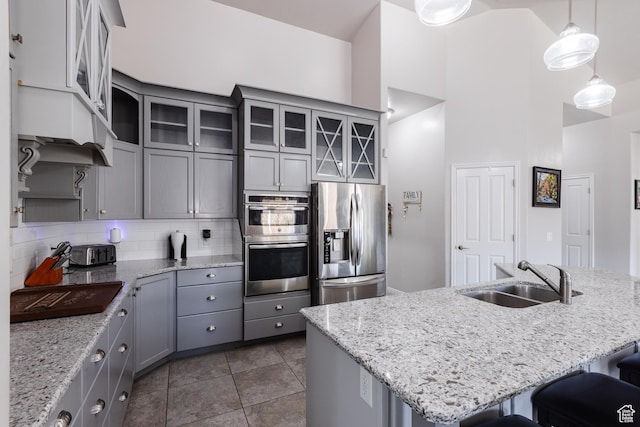 kitchen with a sink, stainless steel appliances, gray cabinets, a breakfast bar, and backsplash