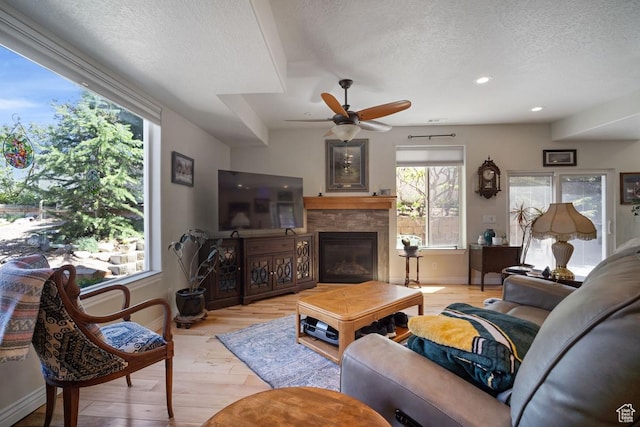 living area with a textured ceiling, light wood-style flooring, a fireplace, baseboards, and recessed lighting