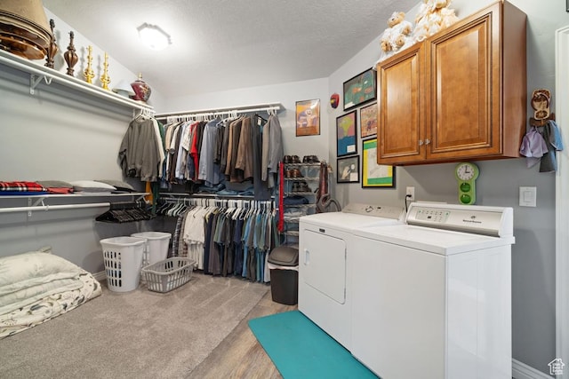 laundry area featuring washer and clothes dryer, cabinet space, light wood finished floors, and a textured ceiling