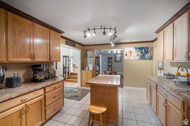kitchen with light tile patterned flooring, a center island, light stone countertops, ornamental molding, and baseboards