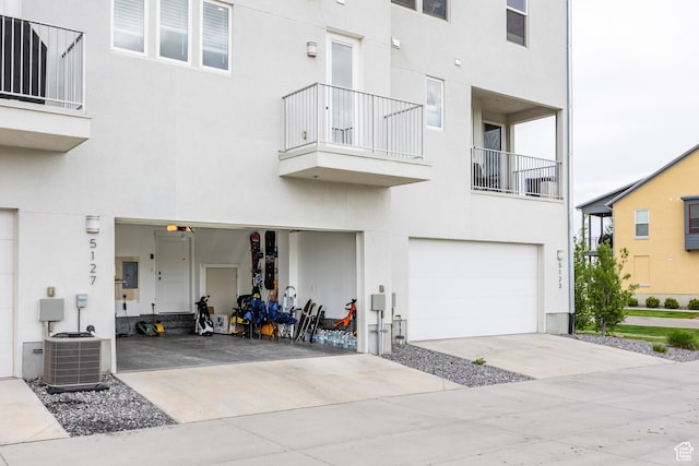 view of front of home featuring a balcony, stucco siding, a garage, central AC unit, and driveway