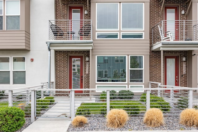 view of exterior entry with brick siding, stucco siding, and fence