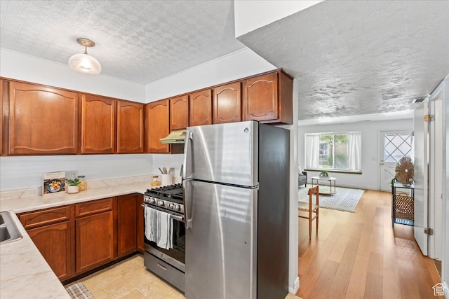 kitchen featuring appliances with stainless steel finishes, under cabinet range hood, light countertops, brown cabinets, and light wood-type flooring