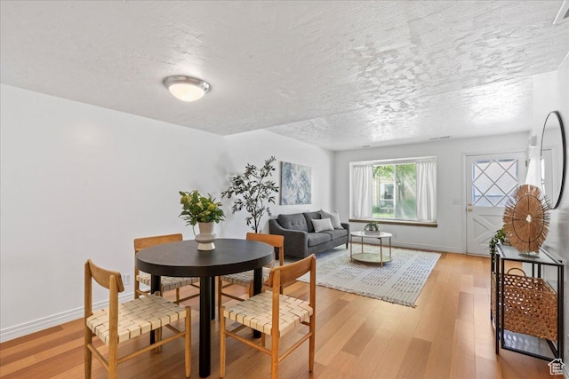 dining room featuring a textured ceiling, light wood finished floors, and baseboards