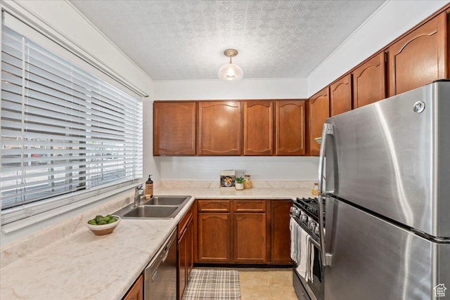 kitchen featuring stainless steel appliances, a sink, light countertops, brown cabinetry, and a textured ceiling