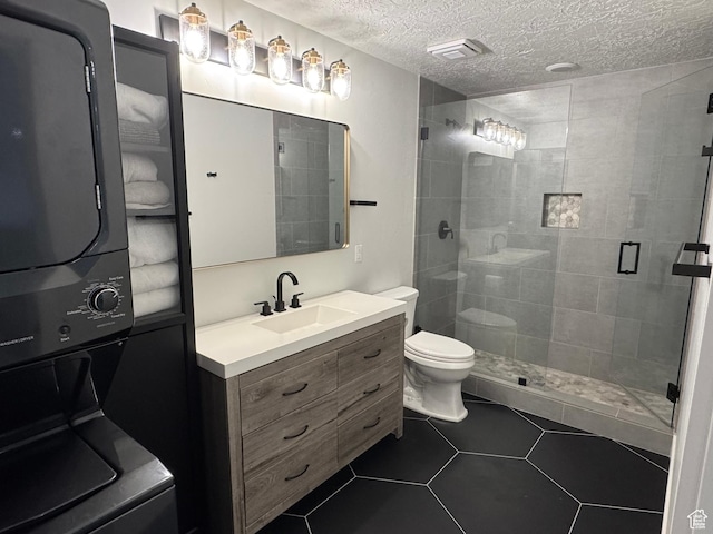 bathroom featuring estacked washer and dryer, a stall shower, toilet, vanity, and a textured ceiling