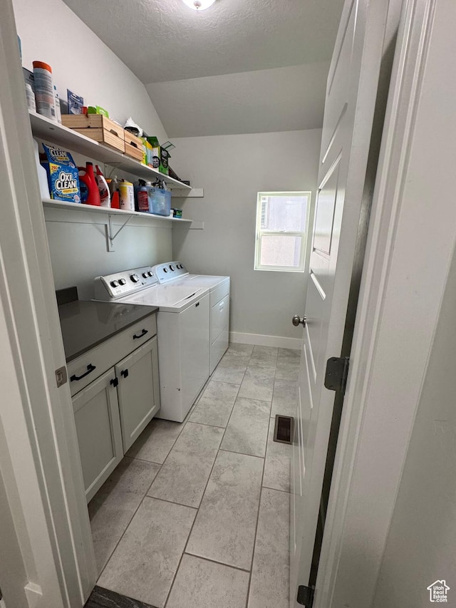 laundry room with washing machine and clothes dryer, a textured ceiling, cabinet space, and baseboards