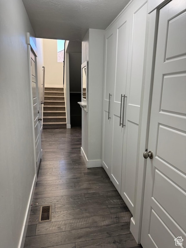 corridor featuring baseboards, dark wood finished floors, and stairway