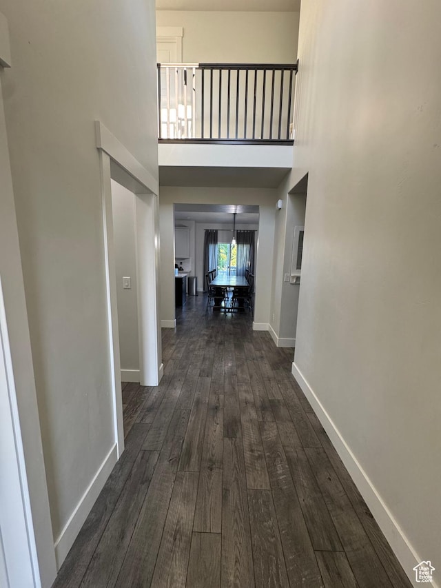 hallway featuring dark wood-type flooring, a towering ceiling, and baseboards
