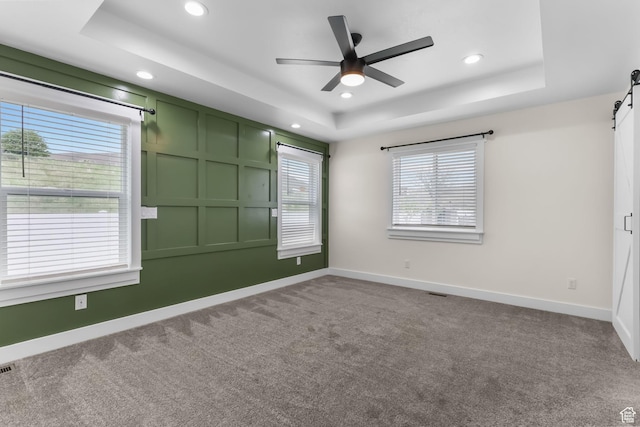 carpeted empty room featuring a tray ceiling, a barn door, recessed lighting, ceiling fan, and baseboards