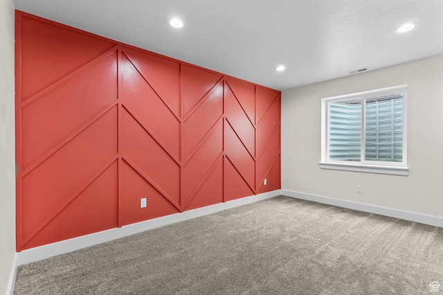 carpeted empty room featuring baseboards, recessed lighting, and a decorative wall