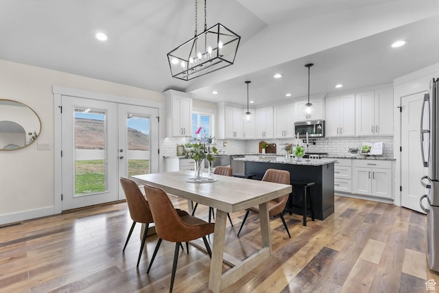 dining room with lofted ceiling, light wood finished floors, recessed lighting, french doors, and a chandelier