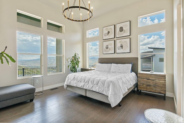 bedroom featuring a chandelier, multiple windows, dark wood finished floors, baseboards, and a towering ceiling