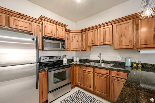 kitchen with appliances with stainless steel finishes, a sink, brown cabinets, and dark stone countertops