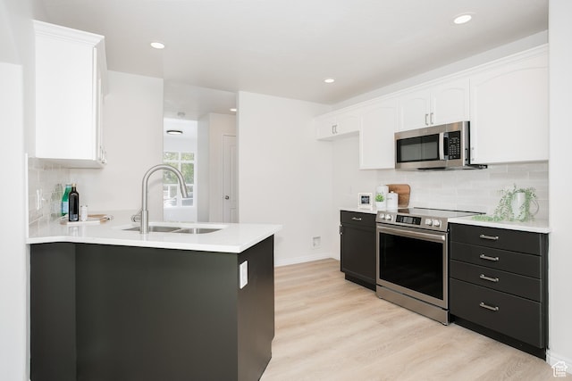 kitchen featuring stainless steel appliances, a sink, white cabinets, light wood-type flooring, and recessed lighting
