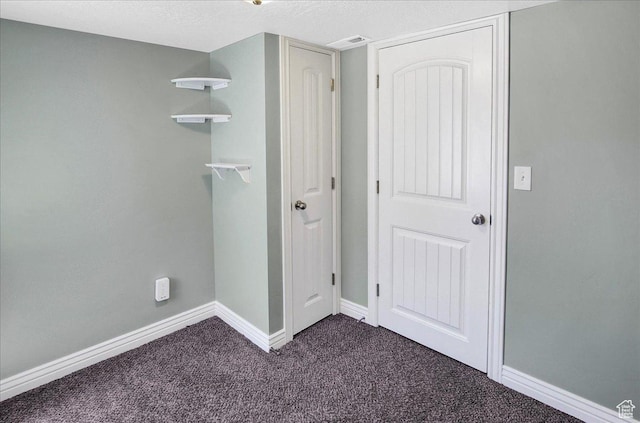 unfurnished bedroom featuring baseboards, dark colored carpet, and a textured ceiling