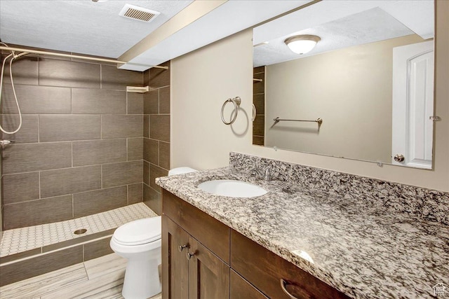 bathroom with tiled shower, toilet, vanity, and a textured ceiling