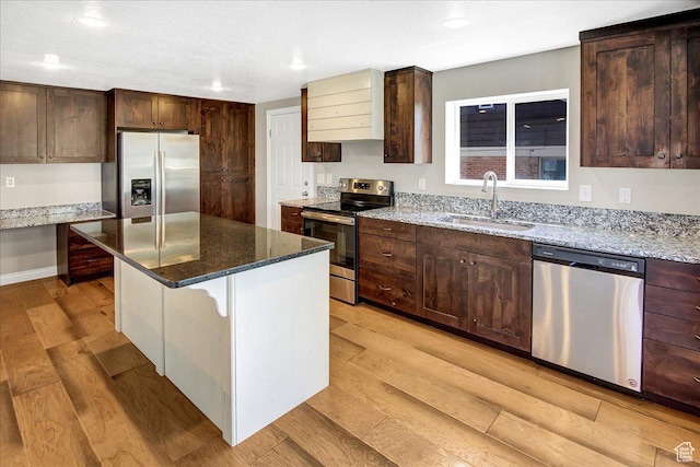 kitchen with stainless steel appliances, a sink, light wood-style floors, light stone countertops, and recessed lighting