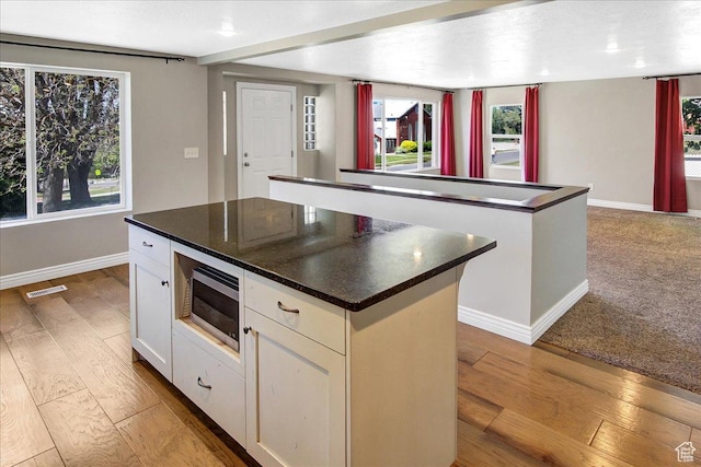 kitchen with a kitchen island, stainless steel microwave, wood-type flooring, dark countertops, and baseboards