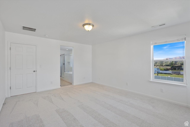 unfurnished bedroom featuring light colored carpet, baseboards, and ensuite bath