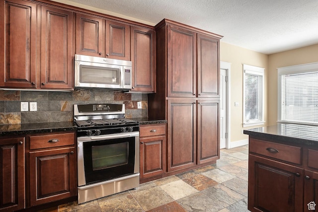 kitchen featuring stainless steel appliances, tasteful backsplash, stone tile floors, a textured ceiling, and baseboards