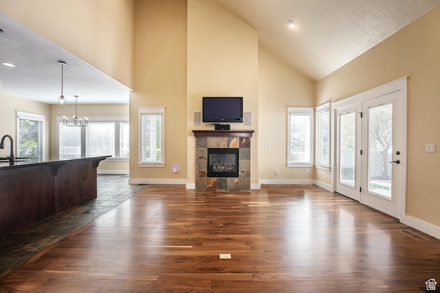 living room with a textured ceiling, a tile fireplace, baseboards, high vaulted ceiling, and dark wood finished floors