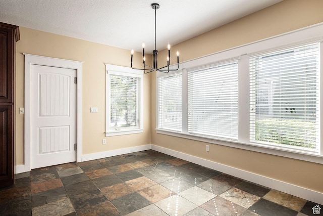 unfurnished dining area with stone tile floors, baseboards, and a chandelier
