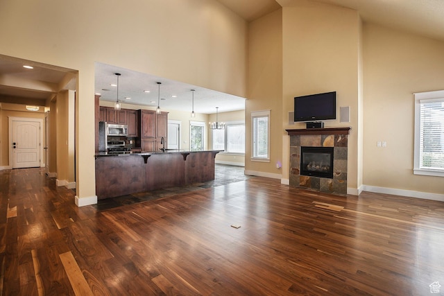 kitchen with high vaulted ceiling, a breakfast bar area, open floor plan, dark wood finished floors, and stainless steel microwave