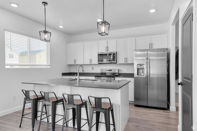 2607 N Mclaws Ave, Layton, UT 84040 - kitchen featuring appliances with stainless steel finishes, a sink, light wood finished floors, a kitchen island with sink, and dark countertops