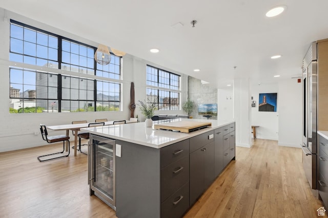 kitchen featuring wine cooler, light wood-style floors, light countertops, a kitchen island, and baseboards