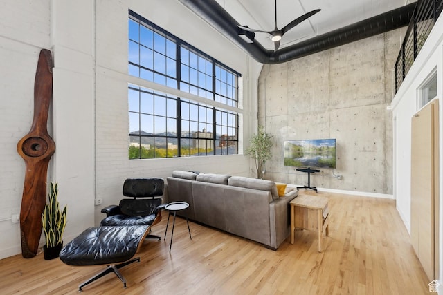 living area featuring wood finished floors, a high ceiling, ceiling fan, and baseboards