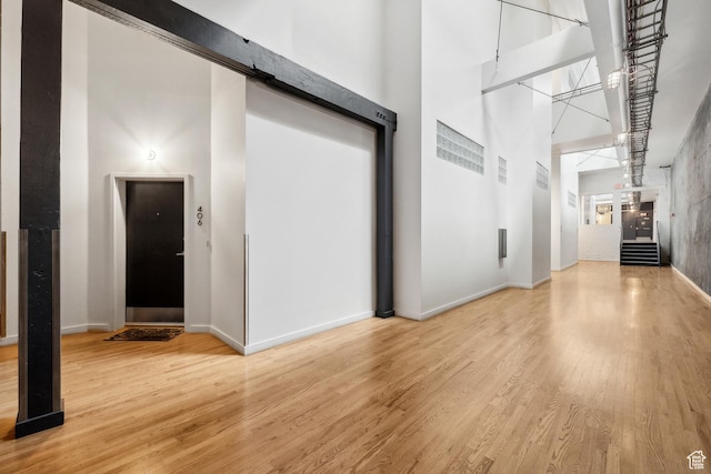 corridor featuring a high ceiling, light wood finished floors, and baseboards