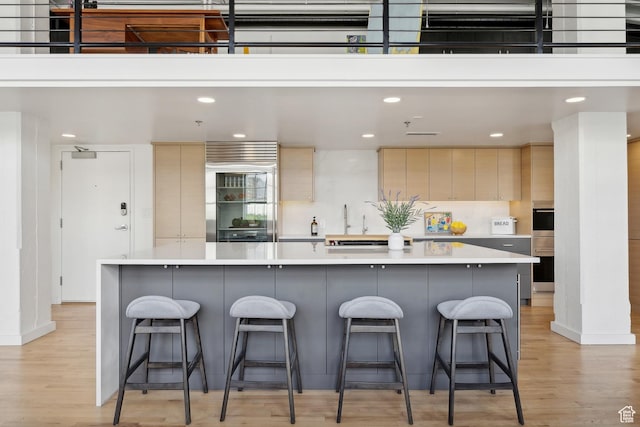 kitchen featuring light wood-style floors, built in refrigerator, light countertops, recessed lighting, and a kitchen bar