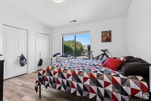 bedroom with light wood-style flooring, two closets, access to outside, and vaulted ceiling