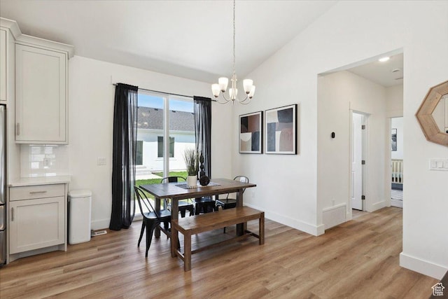 dining room with a chandelier, baseboards, light wood-style floors, and lofted ceiling