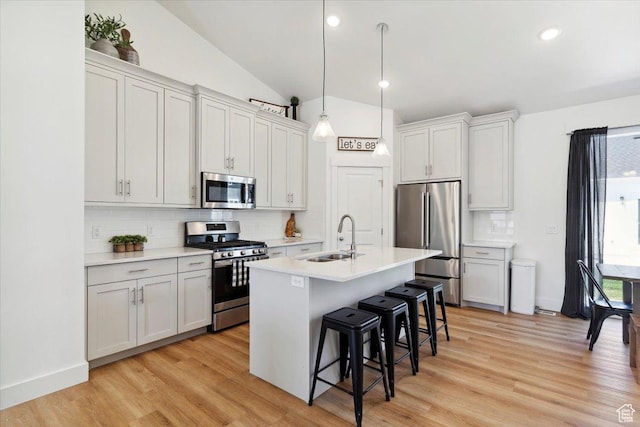 kitchen with appliances with stainless steel finishes, a sink, a kitchen breakfast bar, tasteful backsplash, and vaulted ceiling