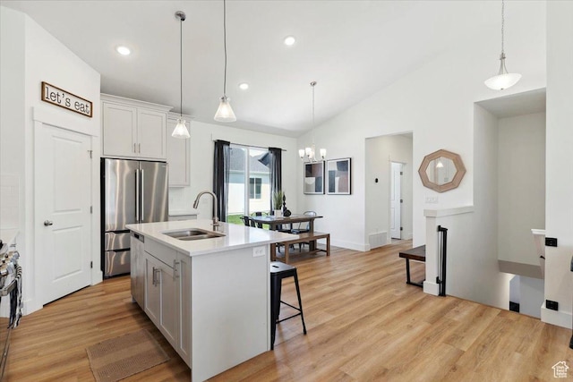 kitchen featuring a sink, freestanding refrigerator, lofted ceiling, a chandelier, and light wood-type flooring
