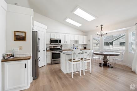kitchen with appliances with stainless steel finishes, lofted ceiling, a kitchen breakfast bar, a chandelier, and tasteful backsplash