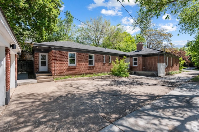 back of house with brick siding, a chimney, driveway, and a patio